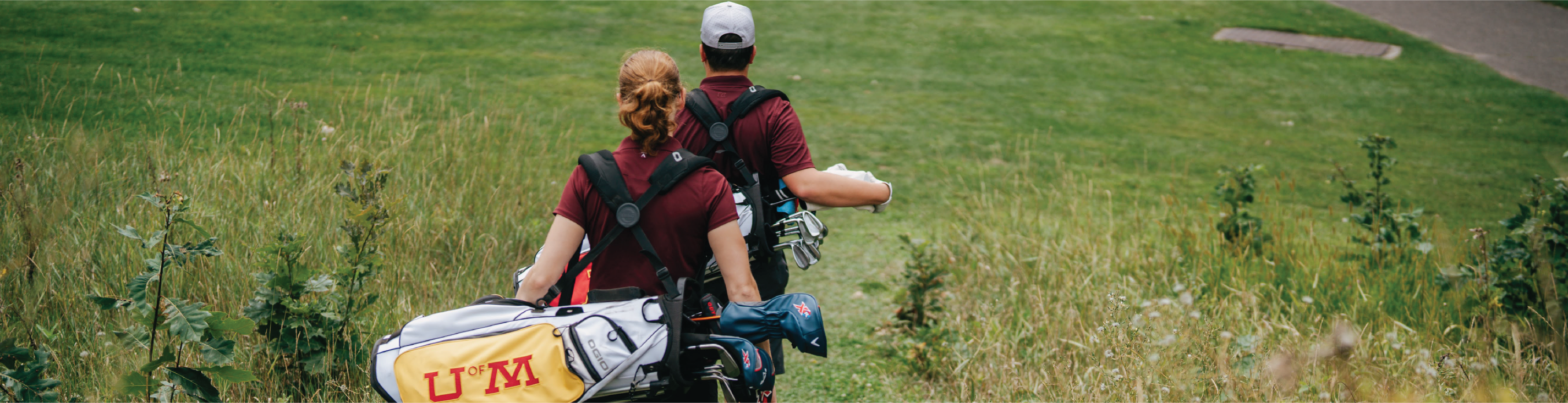 Two golfers walking down grassy hill on course with golf bags on back.